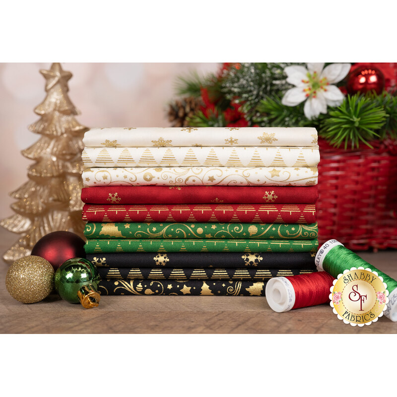 A stack of the holiday-themed fabric included in the Holiday Blenders collection by Timeless Treasures Fabrics, with a basket and a candle and ornaments and thread.