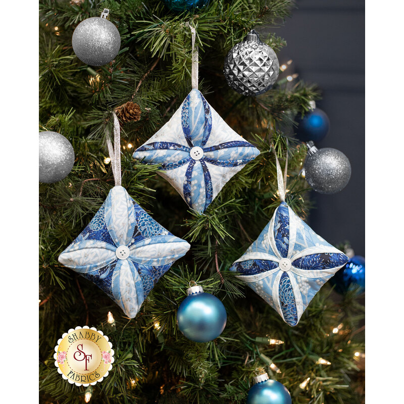 The three completed Cathedral Window Ornaments colored in blue and white fabrics from the Holiday Flourish Festive Finery collection, staged on a decorated Christmas tree.