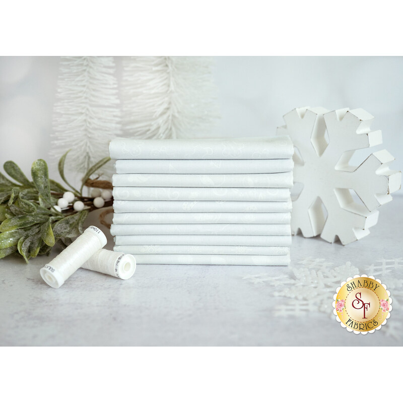 A stack of white fabrics included in the Essentials Stocking Stuffers 2 collection with snowflakes and trees and mistletoe and thread.