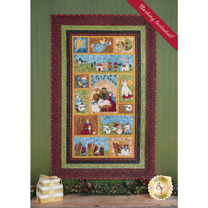 The completed Star of Wonder Panel Quilt, colored in rich red, green, yellow, brown, and blue fabrics, hung on a green paneled wall above a rustic wood table and staged with coordinating winter decor.