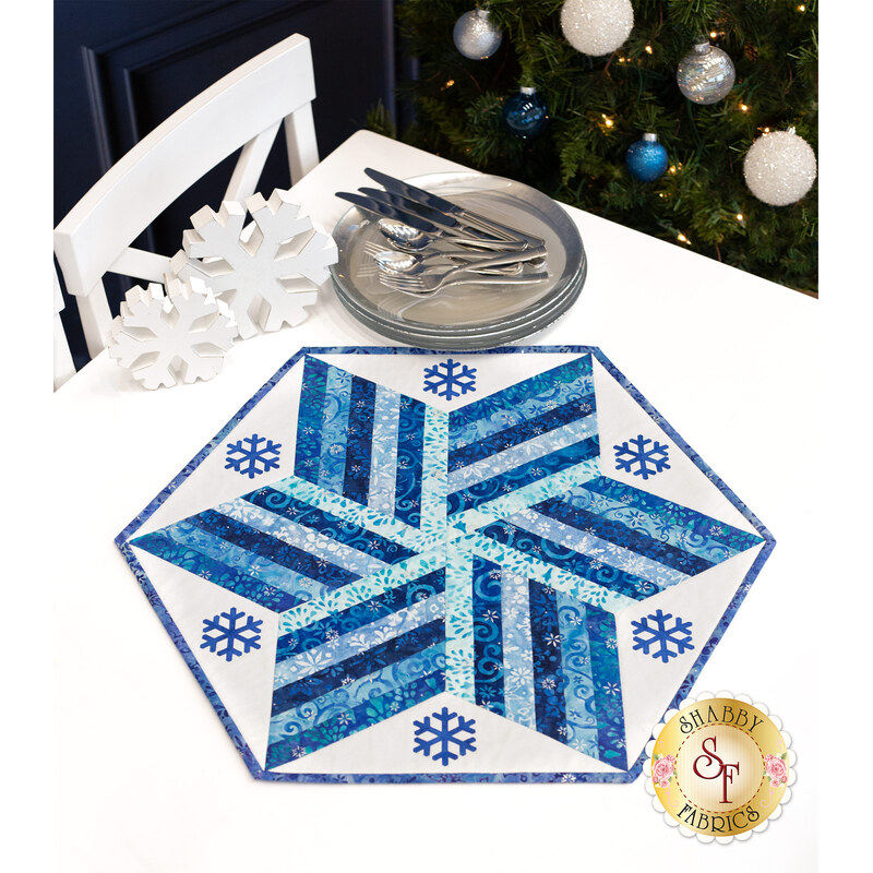 A blue and white star shaped table topper adorned with snowflakes with silver cutlery and snowflake decor.