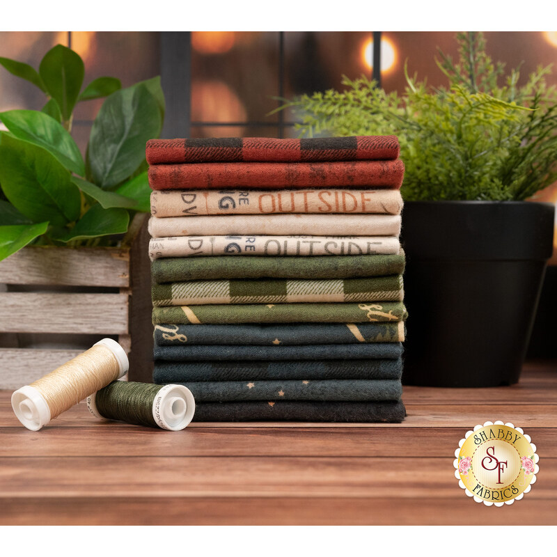 A stack of the fabric included in the Living the Dream Flannel collection, with plants and a window and thread.