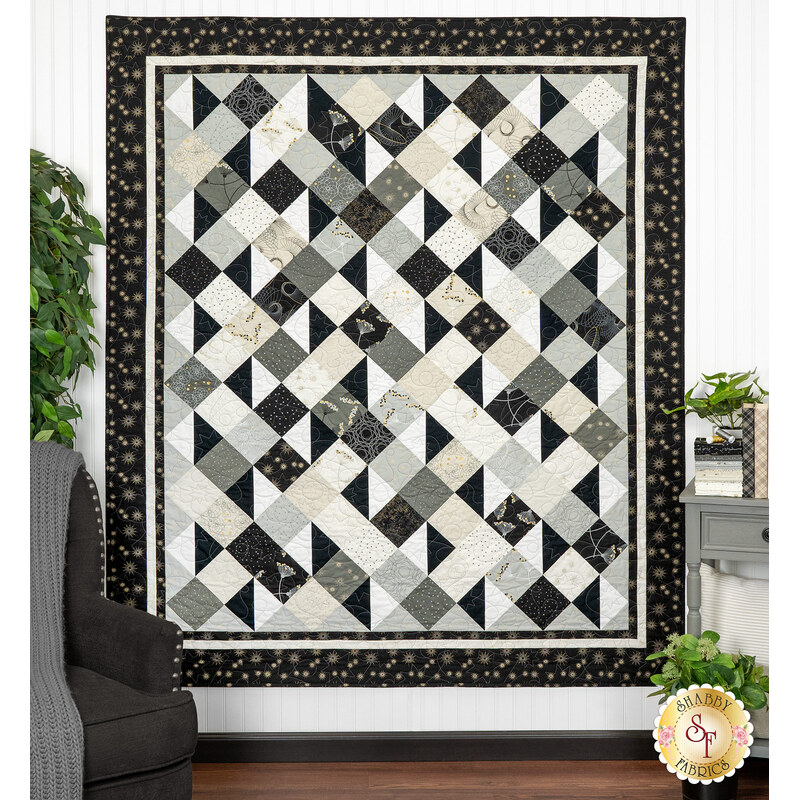 The completed Simply Serene Quilt, colored in neutrals with gold metallic accents from the Shimmer collection by Moda Fabrics, hung on a white paneled wall and staged with coordinating colors.