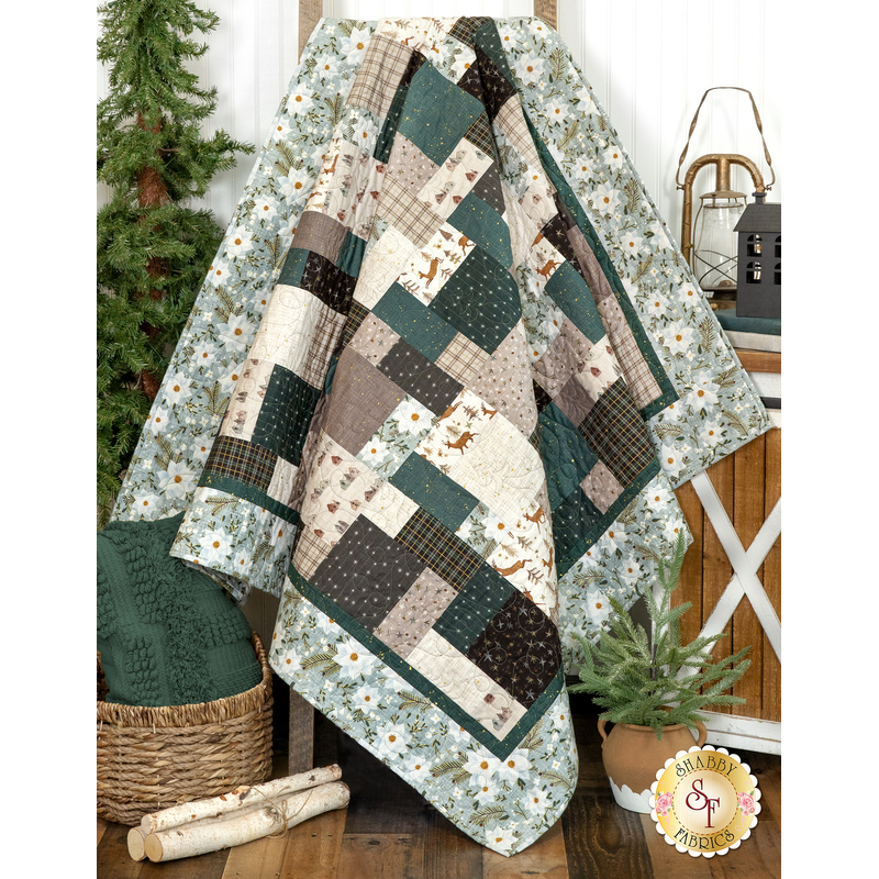 A draped patchwork quilt in muted colors surrounded by greenery and decorative items.