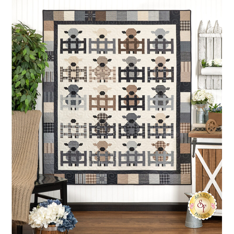 The completed Charming Lambs Quilt in soft and muted fabrics from the Farmhouse Flannels III collection, hung on a white paneled wall and staged with coordinating farmhouse decor.