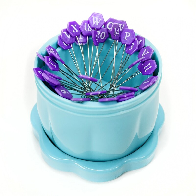 The blue Gypsy Quilter Magnetic Pin Cup opened and full of purple hexagonal-faced quilting pins, isolated on a white background.