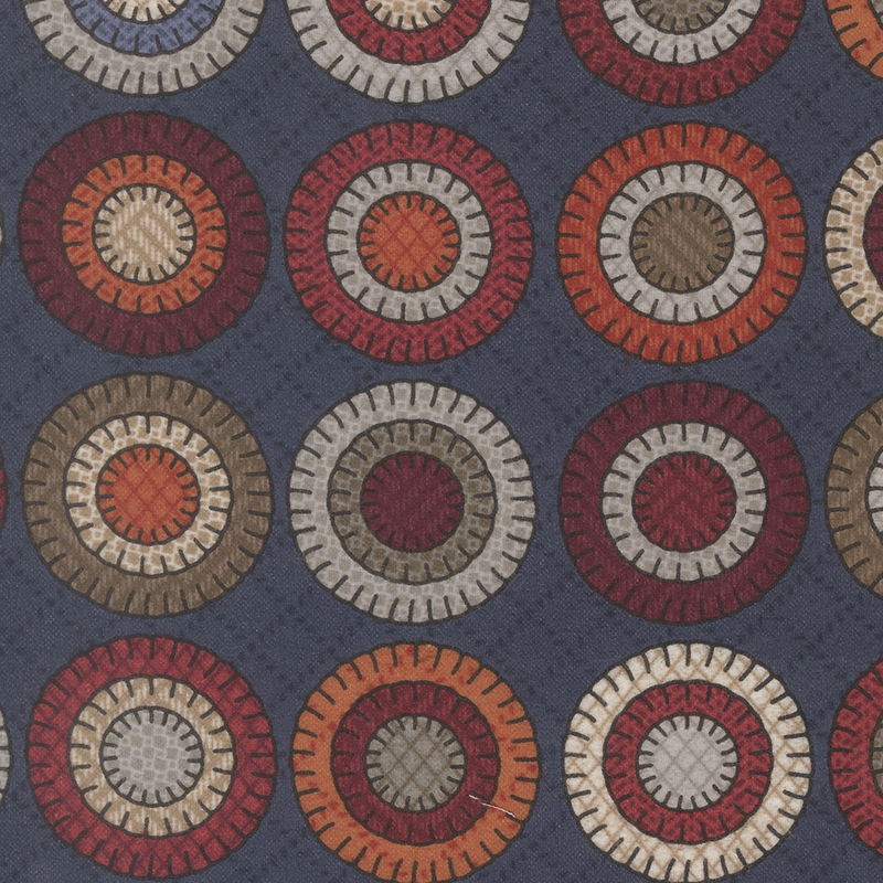 A patterned fabric featuring circular motifs in red, orange, beige, and brown on a dark blue background.