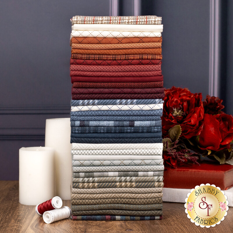 A stack of fabrics in the Prairie Gatherings Flannels Fat Quarter Set featuring various colors and patterns, with flowers, books, candles, and thread.