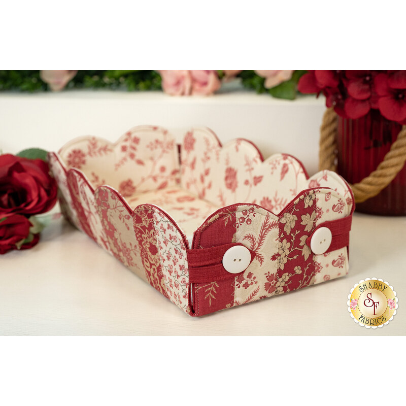 Decorative fabric storage basket with scalloped edges, featuring floral patterns in red and cream.