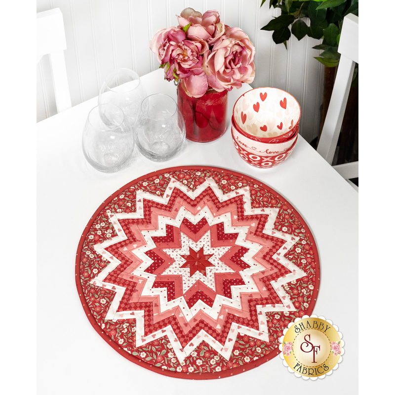 The completed Folded Star Table Topper, colored in red, pink, and white. The topper is staged on a white table with coordinating flowers and seasonal decor.