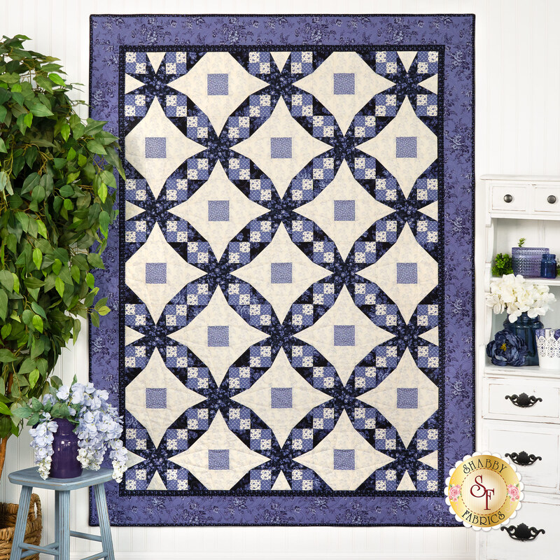 A quilt displaying a geometric pattern of navy blue and cream diamonds, hanging against a light wall.