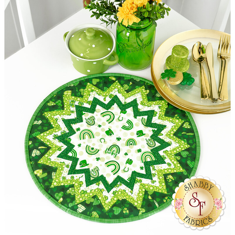 The completed Point of View Folded Star Table Topper colored in white and green fabrics from the Lucky collection. The topper is staged on a white table with coordinating green and gold St. Patrick's Day themed decor.