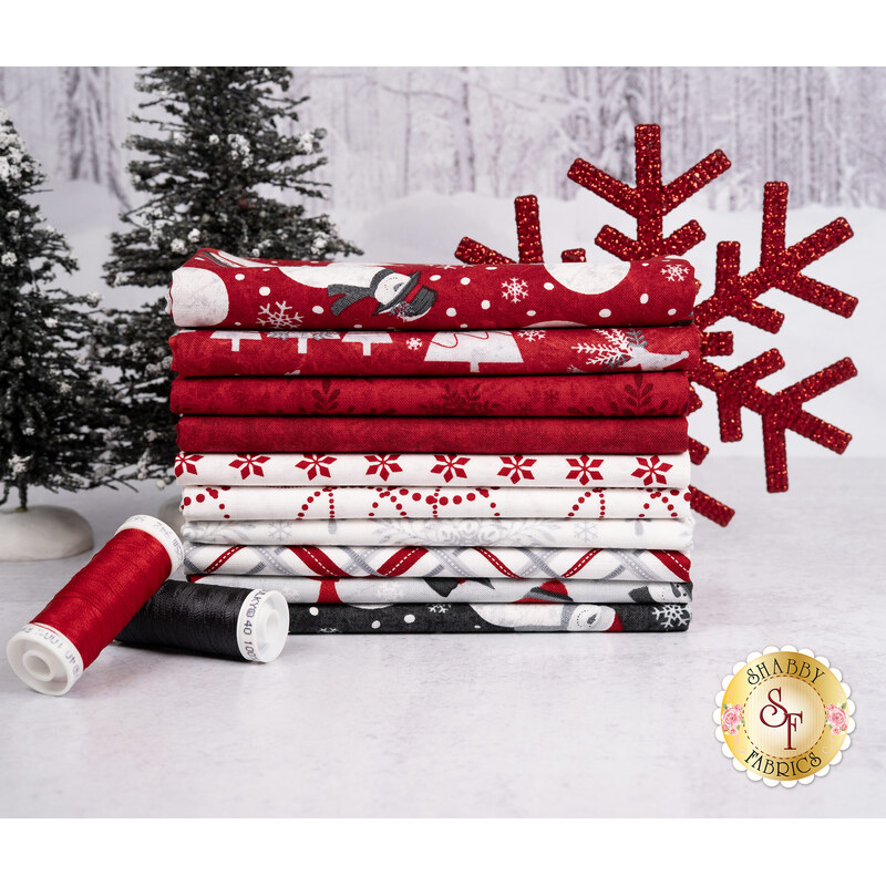 A stack of the fabrics included in the Blizzard Fun, with trees and a snowflake and thread.