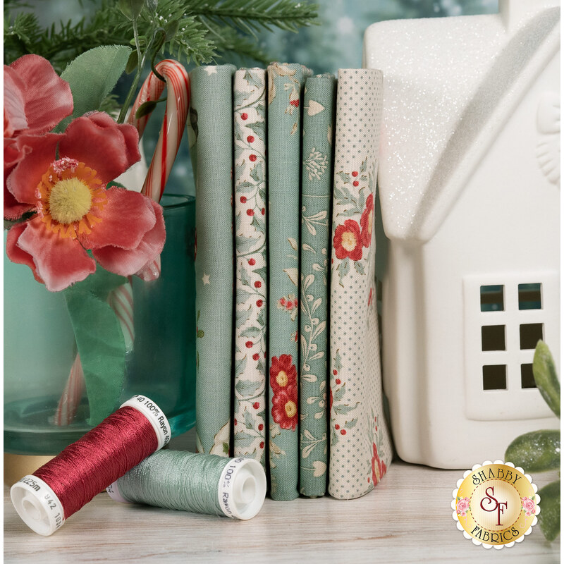 A stack of fabrics featured in the Merry Little Christmas - Duck Egg fat quarter set, with a glass and flowers and a candy cane and a house and thread.