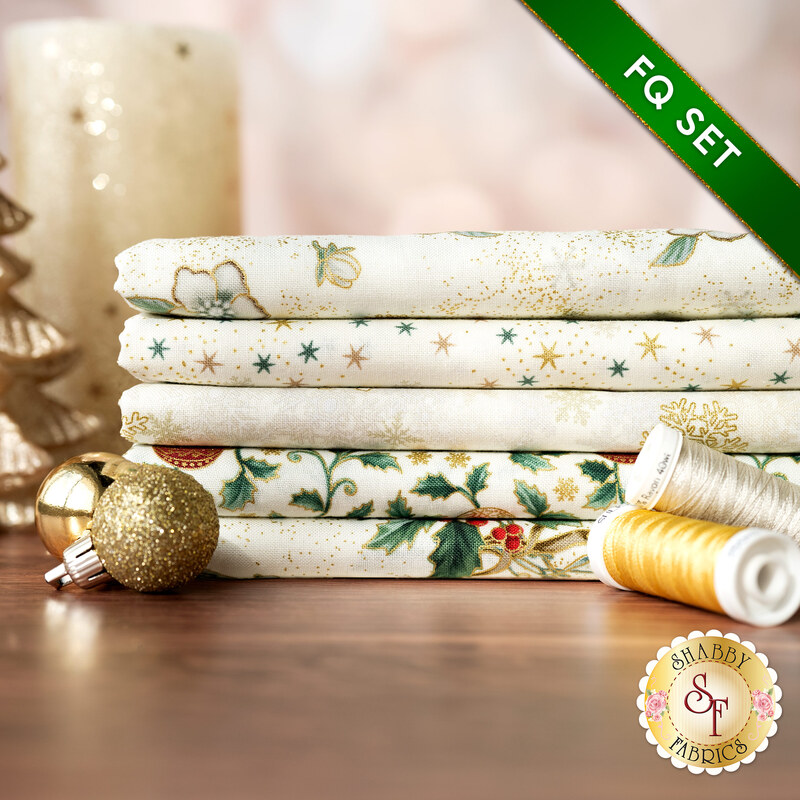 A stack of the fabrics included in the FQ Set Cream/Gold by Stof Fabrics, with candles, ornaments, and thread.