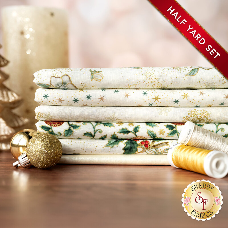 A stack of the six fabrics included in the 6 Half Yard Set Cream/Gold by Stof Fabrics, with candles, ornaments, and thread.