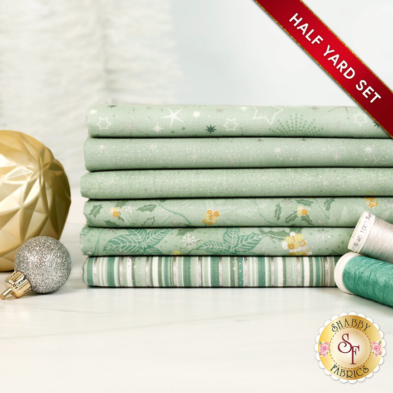 A stack of the six fabrics included in the 6 Half Yard Set Light Mint/Silver by Stof Fabrics, with ornaments and thread.