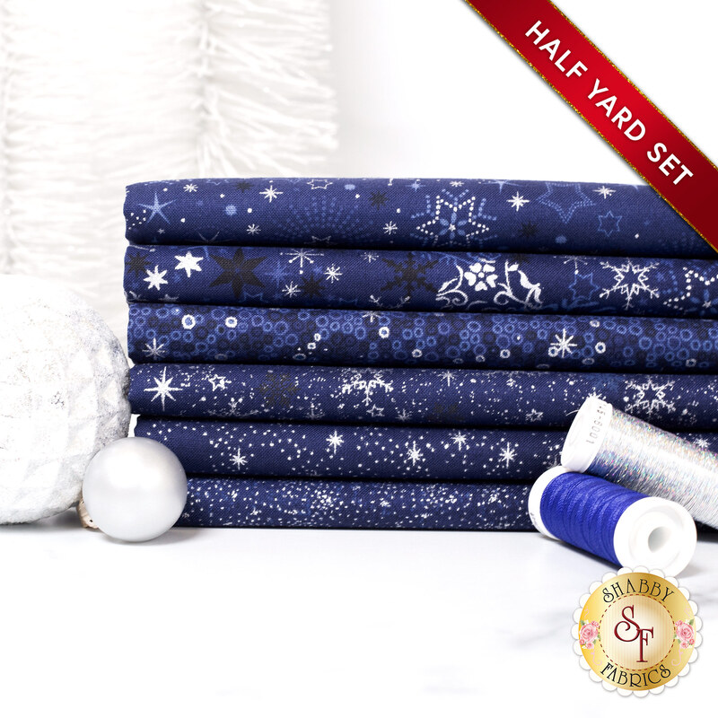 A stack of the six fabrics included in the 6 Half Yard Set Dark Blue/Silver by Stof Fabrics, with ornaments and thread.