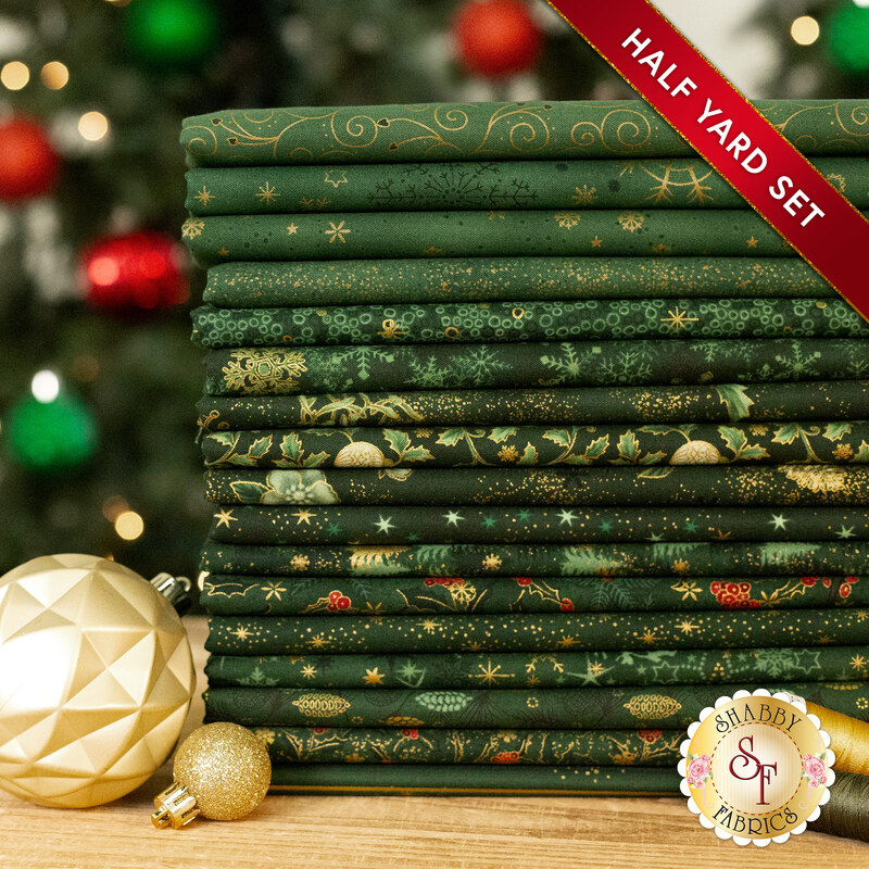 A stack of the seventeen fabrics included in the 17 Half Yard Set Green/Gold by Stof Fabrics, with Christmas trees, thread, and ornaments.