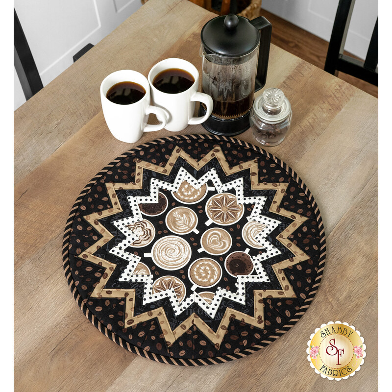 The completed Point of View Folded Star Table Topper, colored in warm browns, espresso, and latte colored prints from the Coffee Life collection, staged atop a wooden table beside two mugs of coffee and a French press.