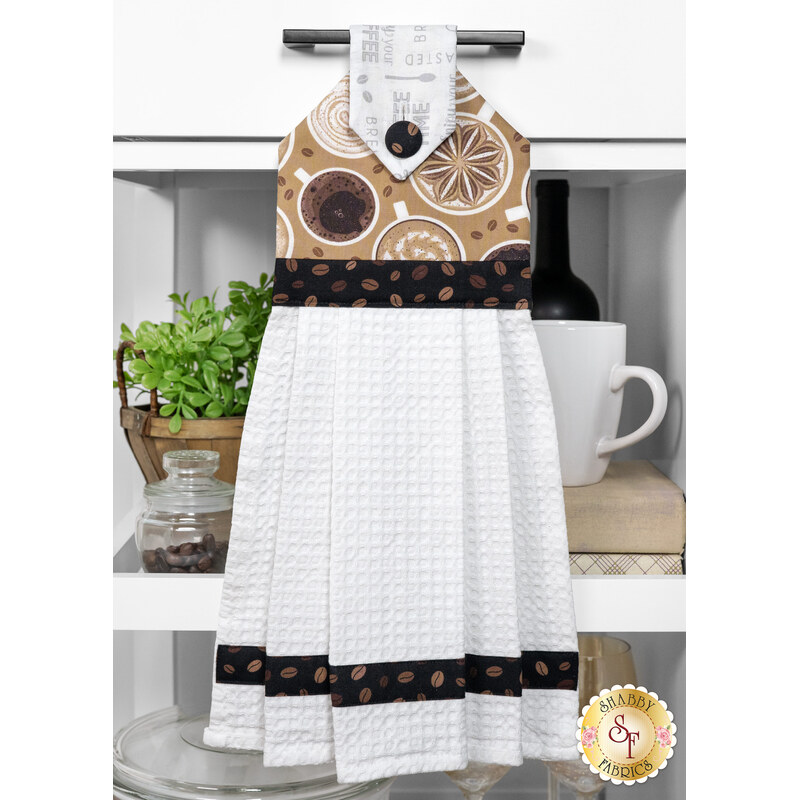 The completed Hanging Towel colored in latte brown fabrics from the Coffee Life collection, staged on a kitchen drawer with coordinating decor.