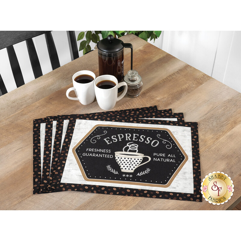 The four completed Self-Binding Placemats, colored in warm browns, espresso, and latte colored prints from the Coffee Life collection and fanned out atop a wooden table beside two mugs of coffee and a French press.