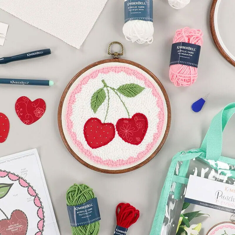 Embroidery hoop featuring a cherry design, surrounded by crafting supplies.