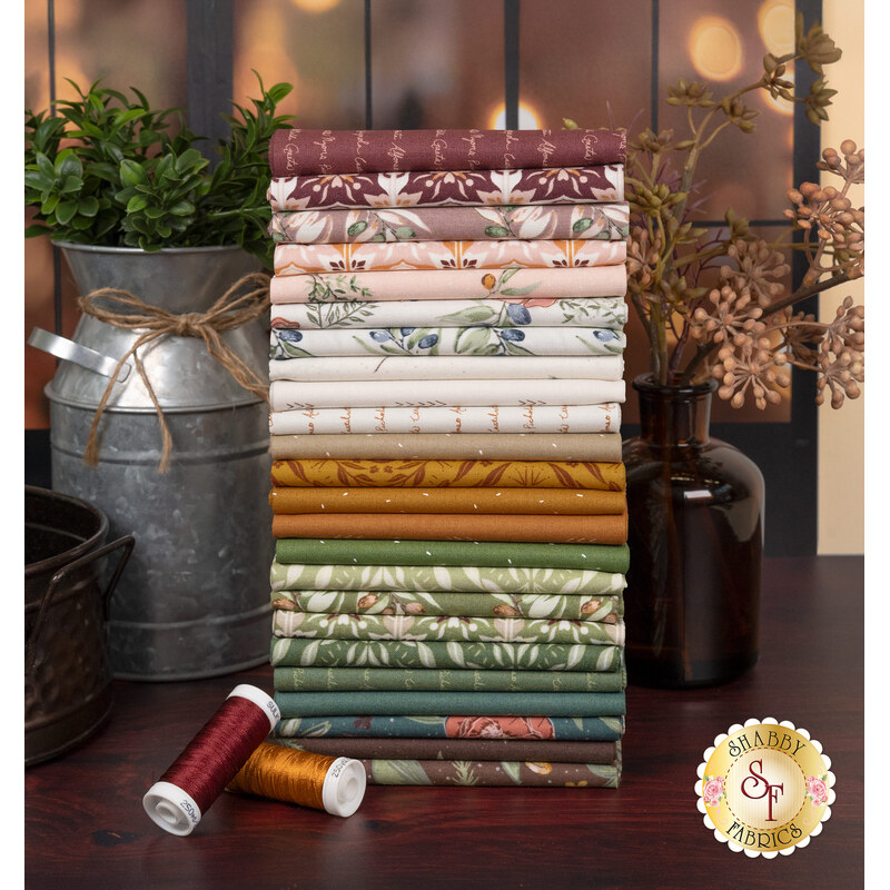 A stack of the fabrics included in the Olive Grove FQ set, with a window and milk jug and plans and thread.