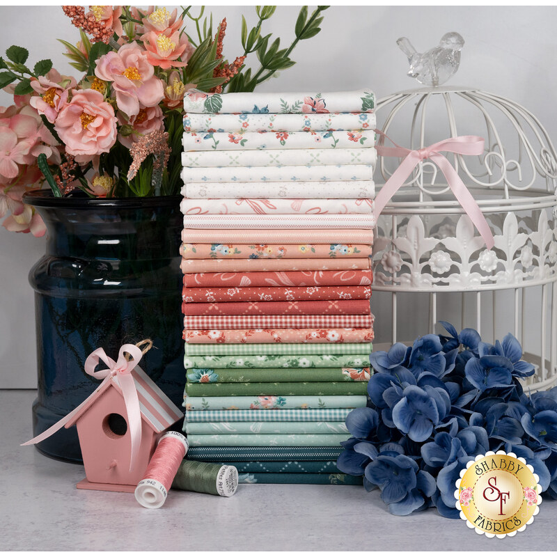 A stack of the fabrics included in the Mary Catherine FQ set, with flowers and a vase and birdcage and a bird house and thread. 