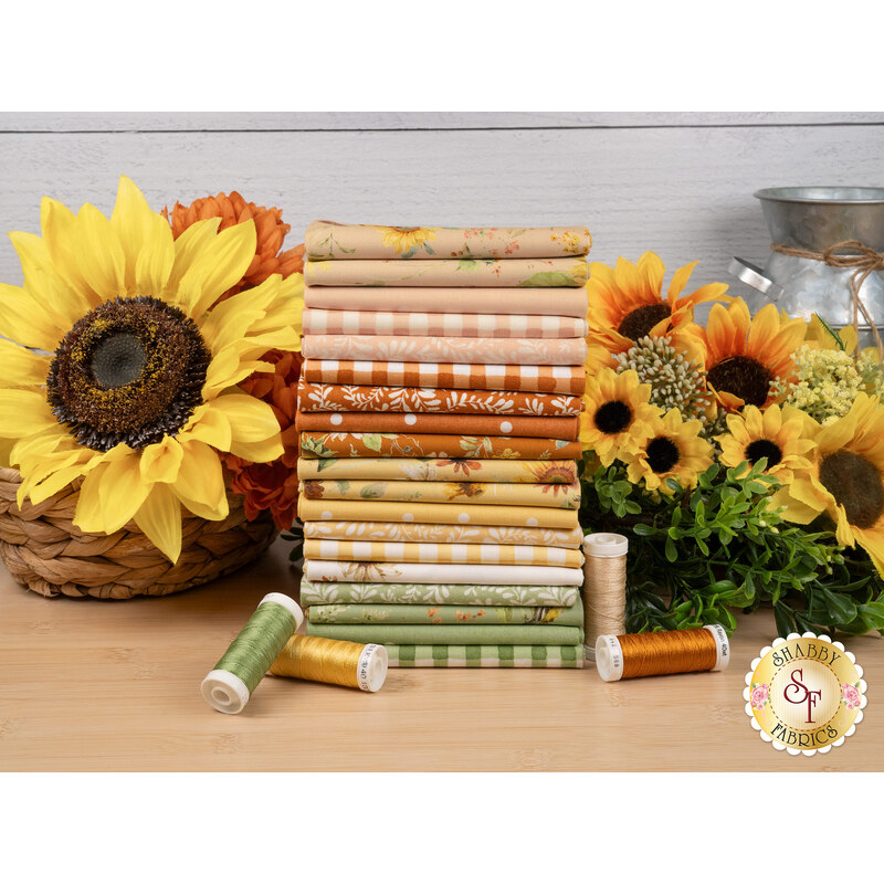 A stack of fabrics included in the Sunflower Whispers FQ set, with sunflowers and a basket and a tin and thread.