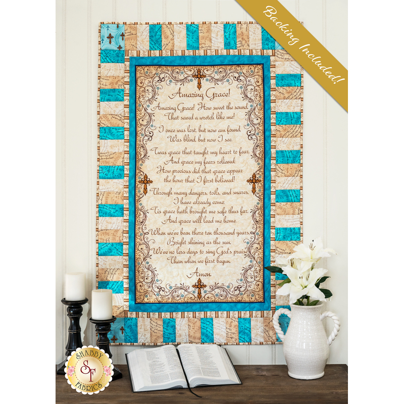 Cream, beige, and aqua colored quilt featuring a script of the Amazing Grace, hung on a cream paneled wall and staged with a bible and coordinating decor.