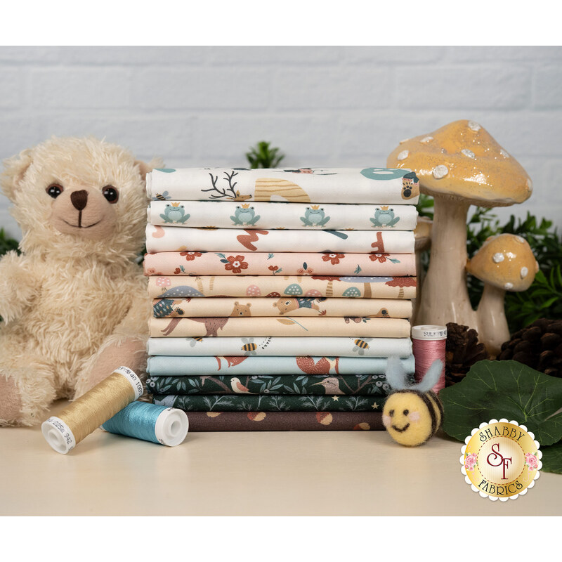 A stack of the fabrics included in the Alphabet City FQ set, with mushrooms and plants and a teddy bear and a bumblebee and thread.