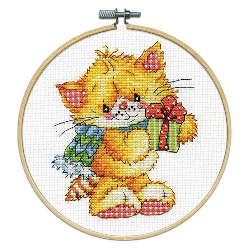 A cross stitch of a cute orange cat holding a small gift, framed in a wooden embroidery hoop