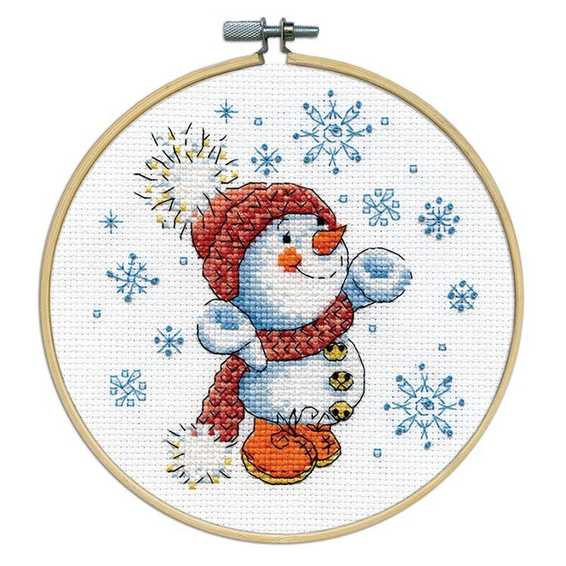 A cross-stitched snowman wearing a red hat and scarf, surrounded by blue snowflakes, framed in a wooden embroidery hoop