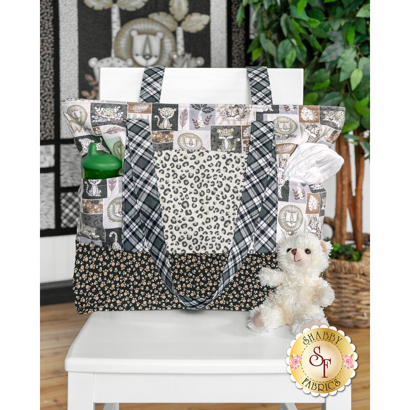 A patterned tote bag featuring animal prints with a green water bottle, tissues, and a plush teddy bear on a chair.