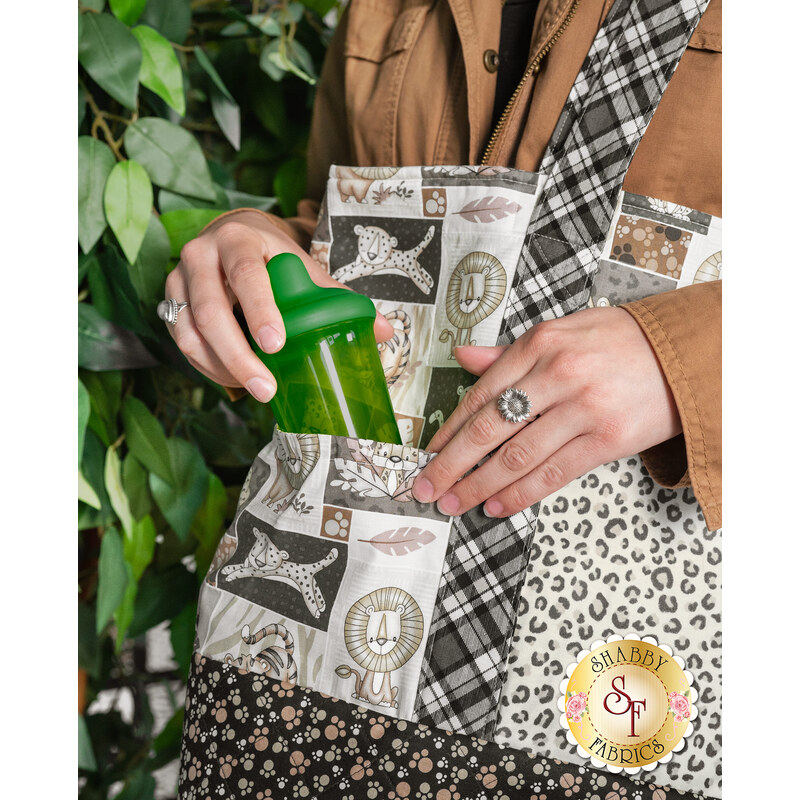 A person grabbing a green water bottle out of a patchwork bag featuring animal designs and patterns.