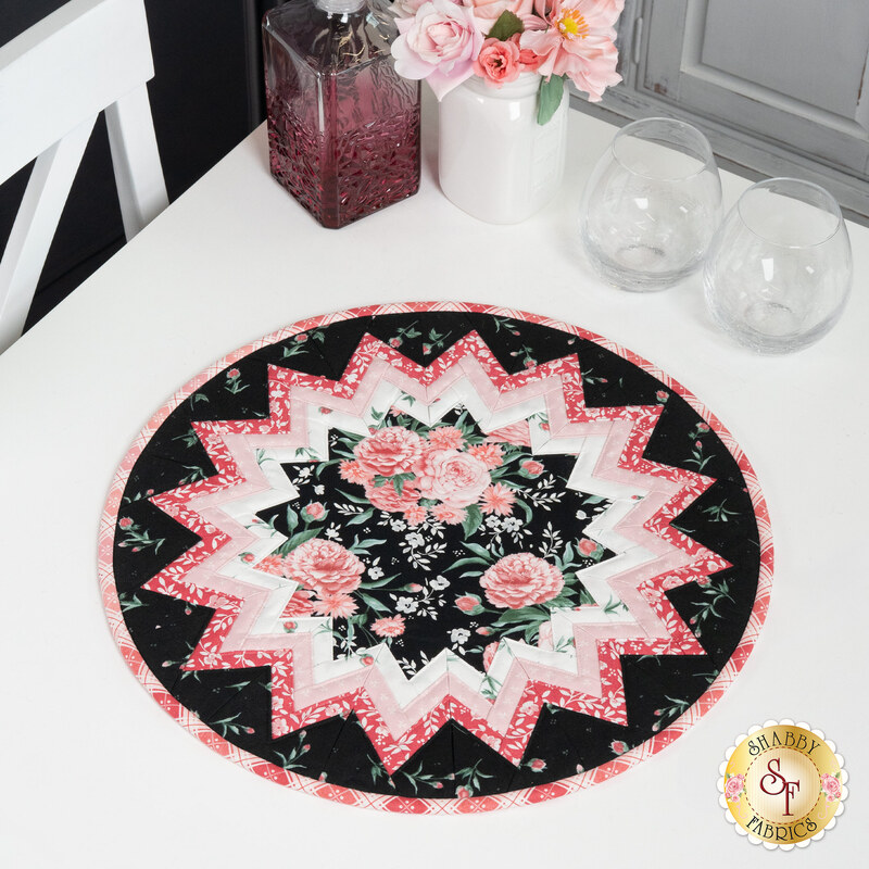 The completed Point of View Folded Star Table Topper colored in pink, black, and white fabrics from the Garden Picnic collection. The topper is staged on a white table with coordinating pink decor.
