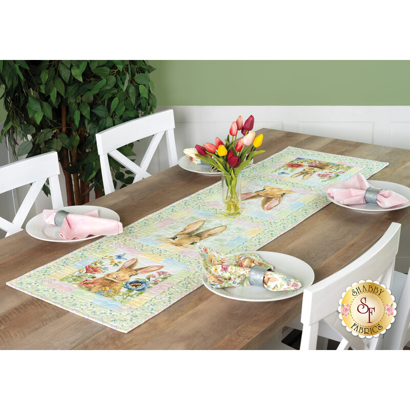 A dining table set with a colorful bunny-themed table runner, plates, and a vase of tulips.