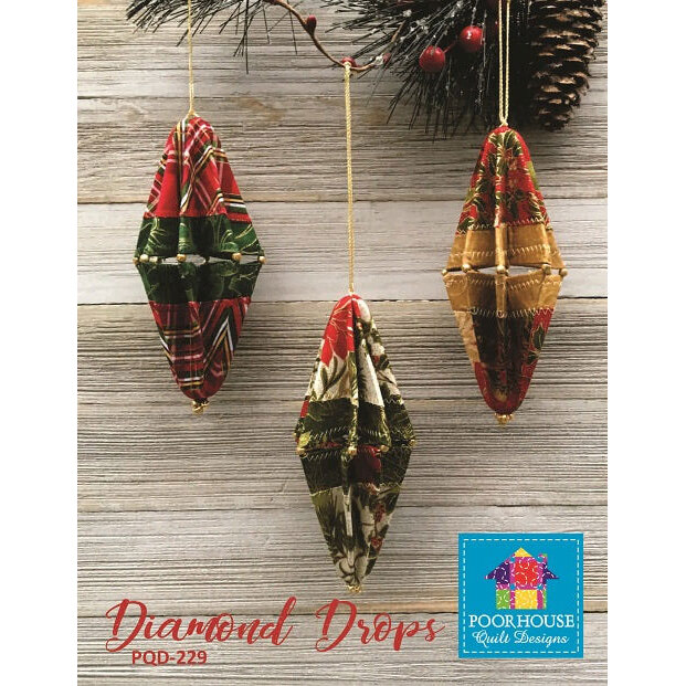 Three diamond-shaped ornaments in festive fabrics hang from a string against a wooden background.