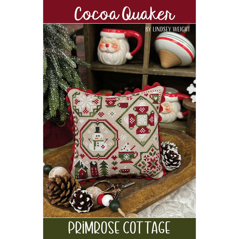 A decorative cushion featuring intricate cross-stitch patterns in red and green, labeled Cocoa Quaker.