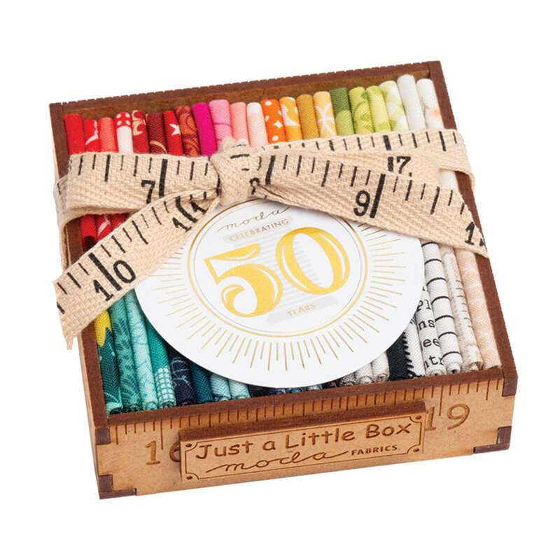 An angled shot of the Celebrating 50 Years of Moda Little Wood Box, with small strips of each SKU in the collection wrapped with a ruler bow.