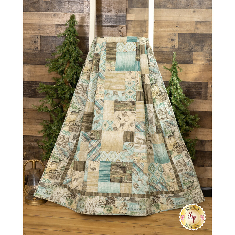 The Easy as ABC and 123 Quilt - Nature's Landscapes quilt featuring a patchwork design in neutral tones hanging from a wooden ladder next to green trees in front of a wood paneled wall.