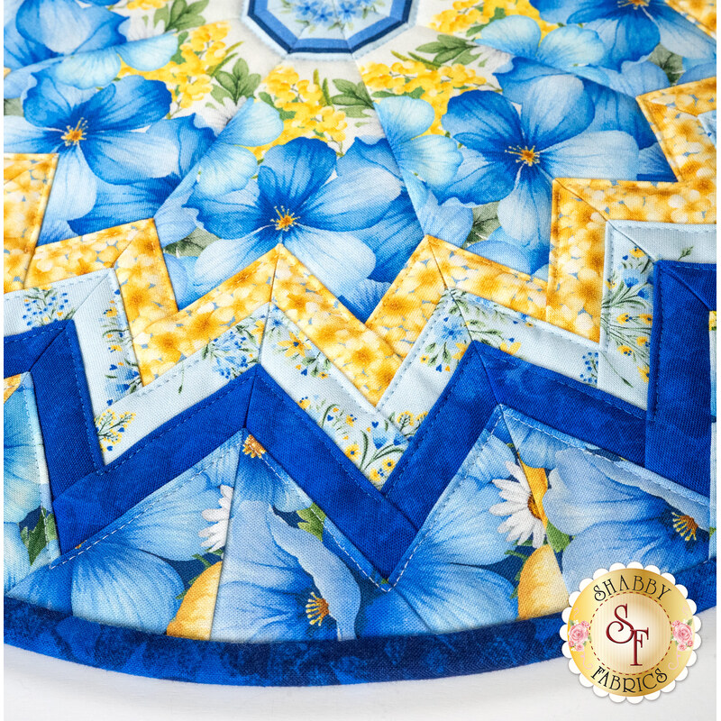 Up close of a circular table topper quilt featuring blue and yellow flowers and star-shaped designs.
