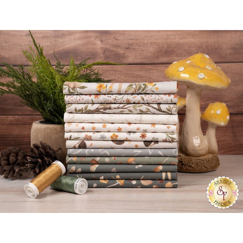 A stack of the fabrics included in the Count On Me collection, with mushrooms and plants and pinecones and thread.