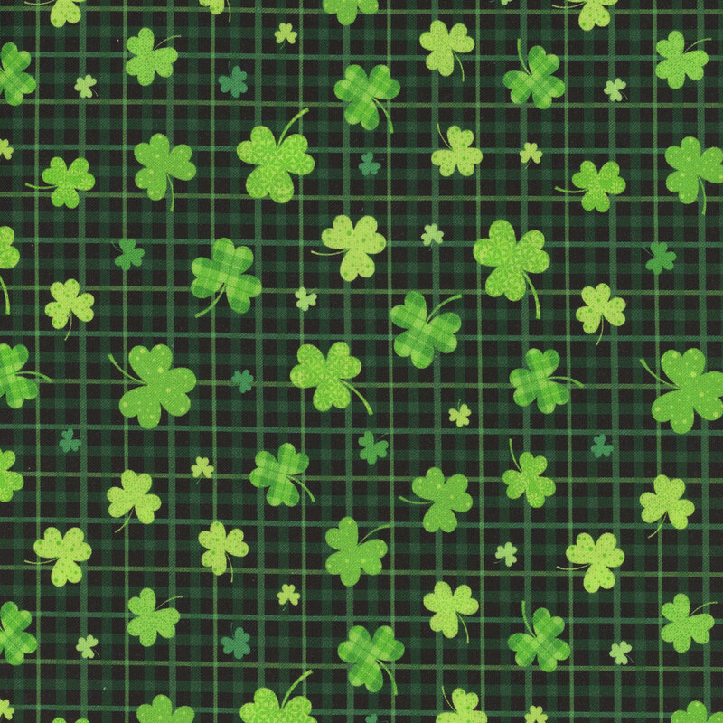 Black fabric with tossed shamrocks on a plaid background.