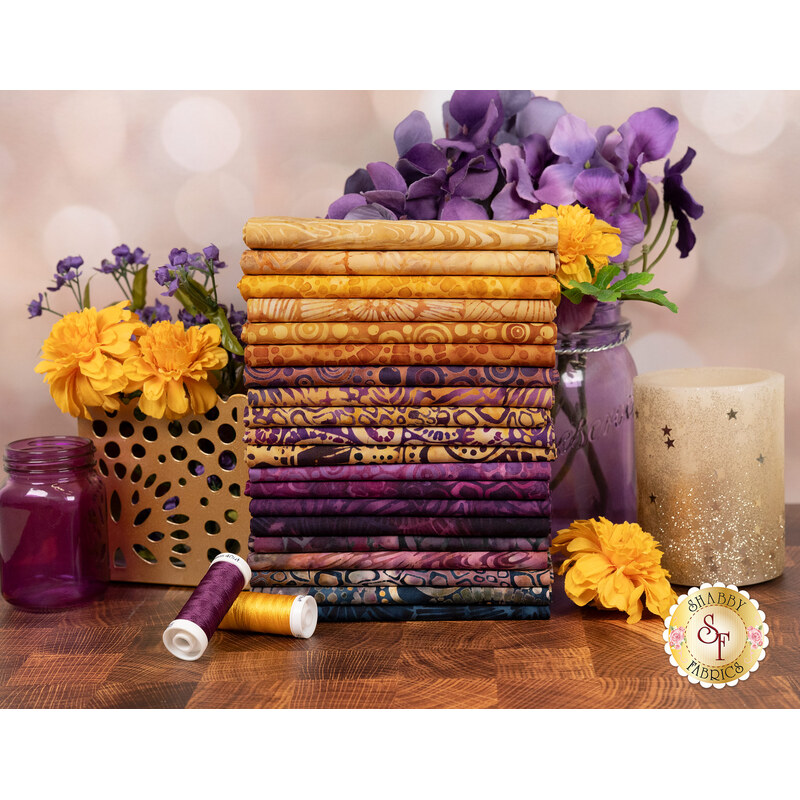 A stack of the fabrics included in the Geode Glow collection, with flowers and jars and candles and thread.