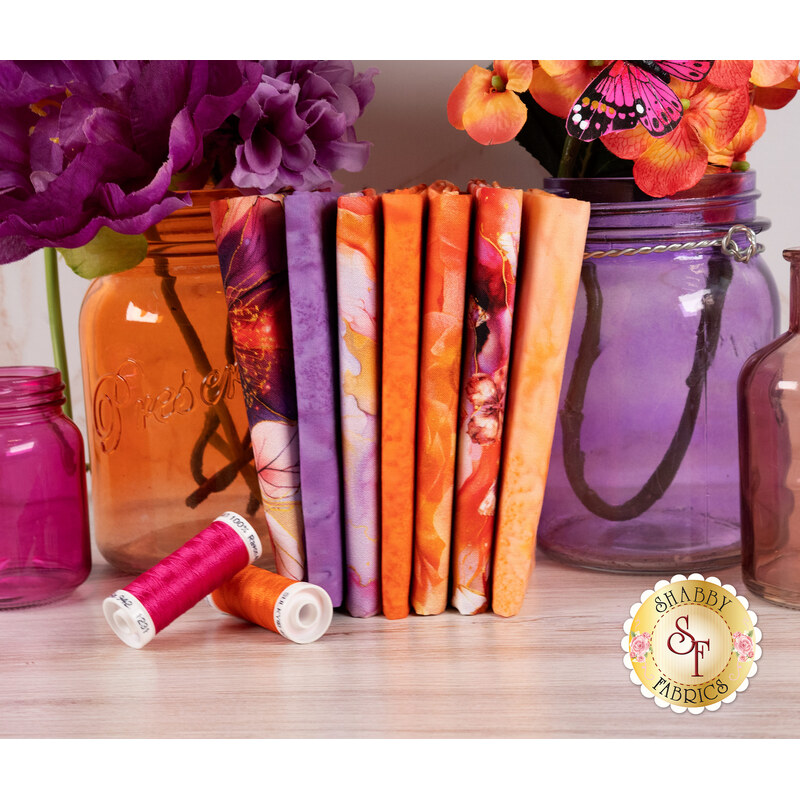 A stack of the fabrics in the Flourish Sunset FQ set with jars and flowers and thread.
