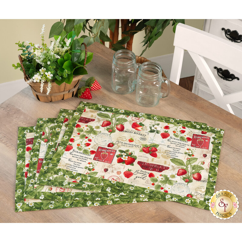 A shot of the four completed strawberry-themed overlapping placemats in the text-and-lemons with butterflies print, staged on a wood table with coordinating table decor and flowers.
