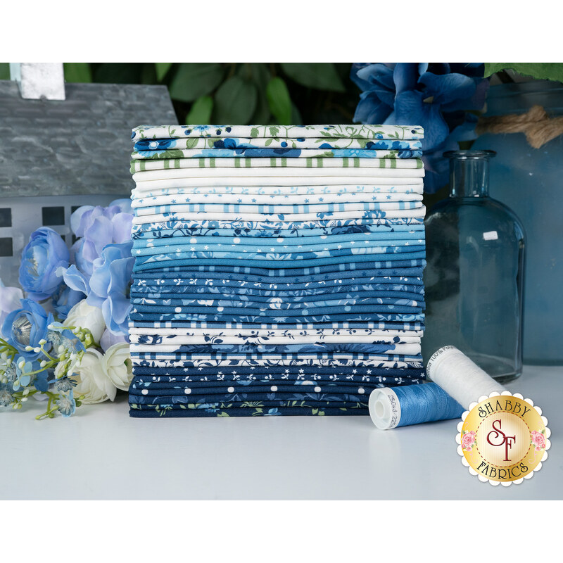 A stack of the fabrics featured in the Blueprint F8 set, with a metal house and flowers and vases and thread.