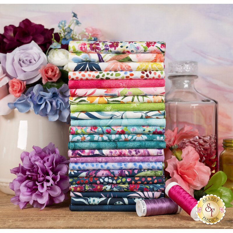 A stack of the fabrics in the Soulstice Fat Quarter Set with flowers and vases and a decanter and thread
